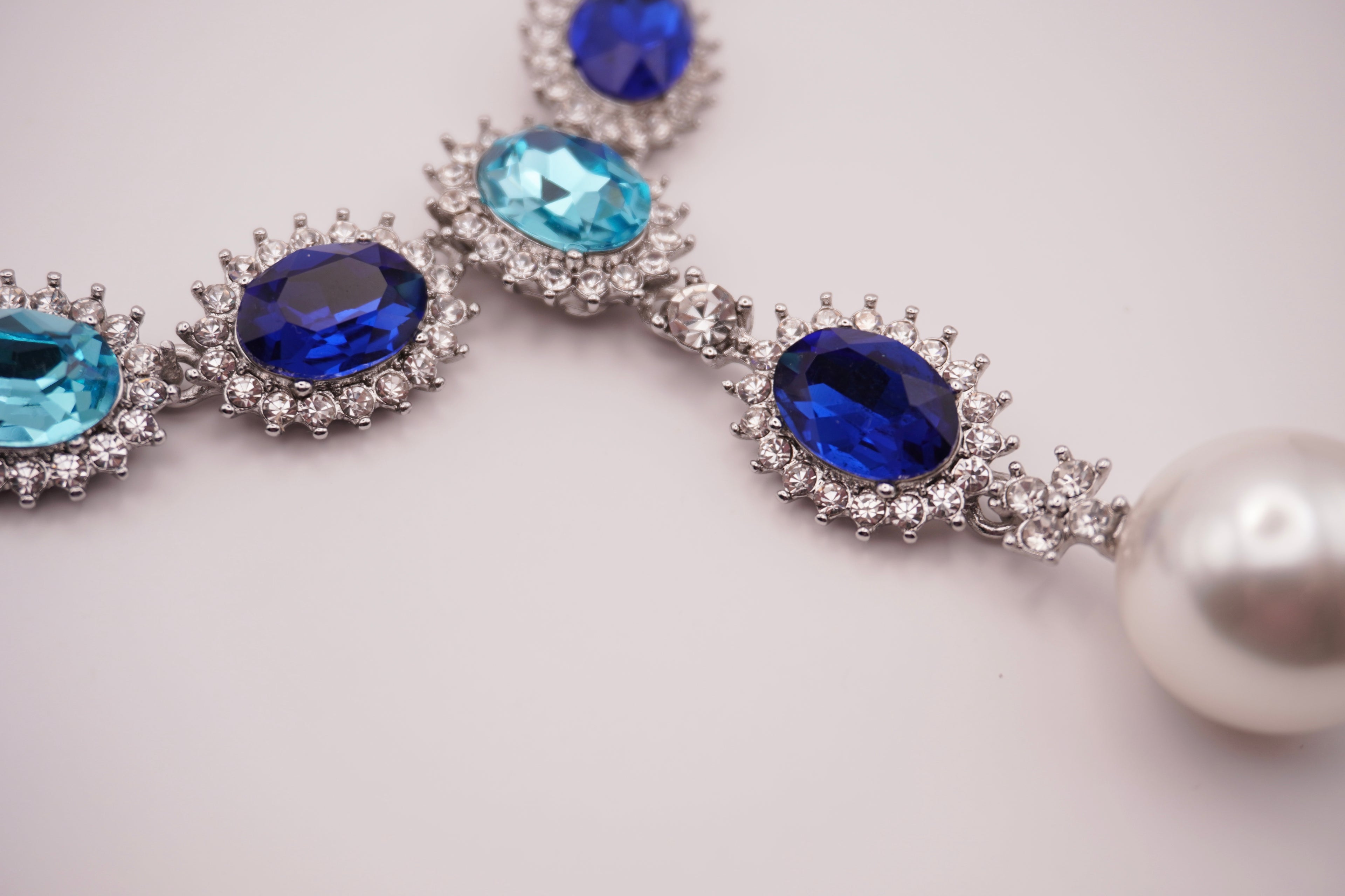 Necklace with blue gemstones and a pearl on a light gray background